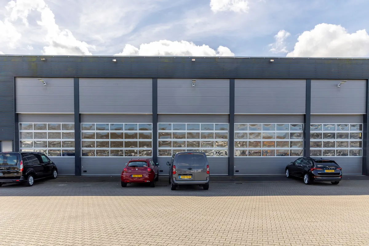 Werkplaats van Van Pelt Auto&rsquo;s in Zuid-Holland met grote glazen overheaddeuren en geparkeerde voertuigen op het voorplein.