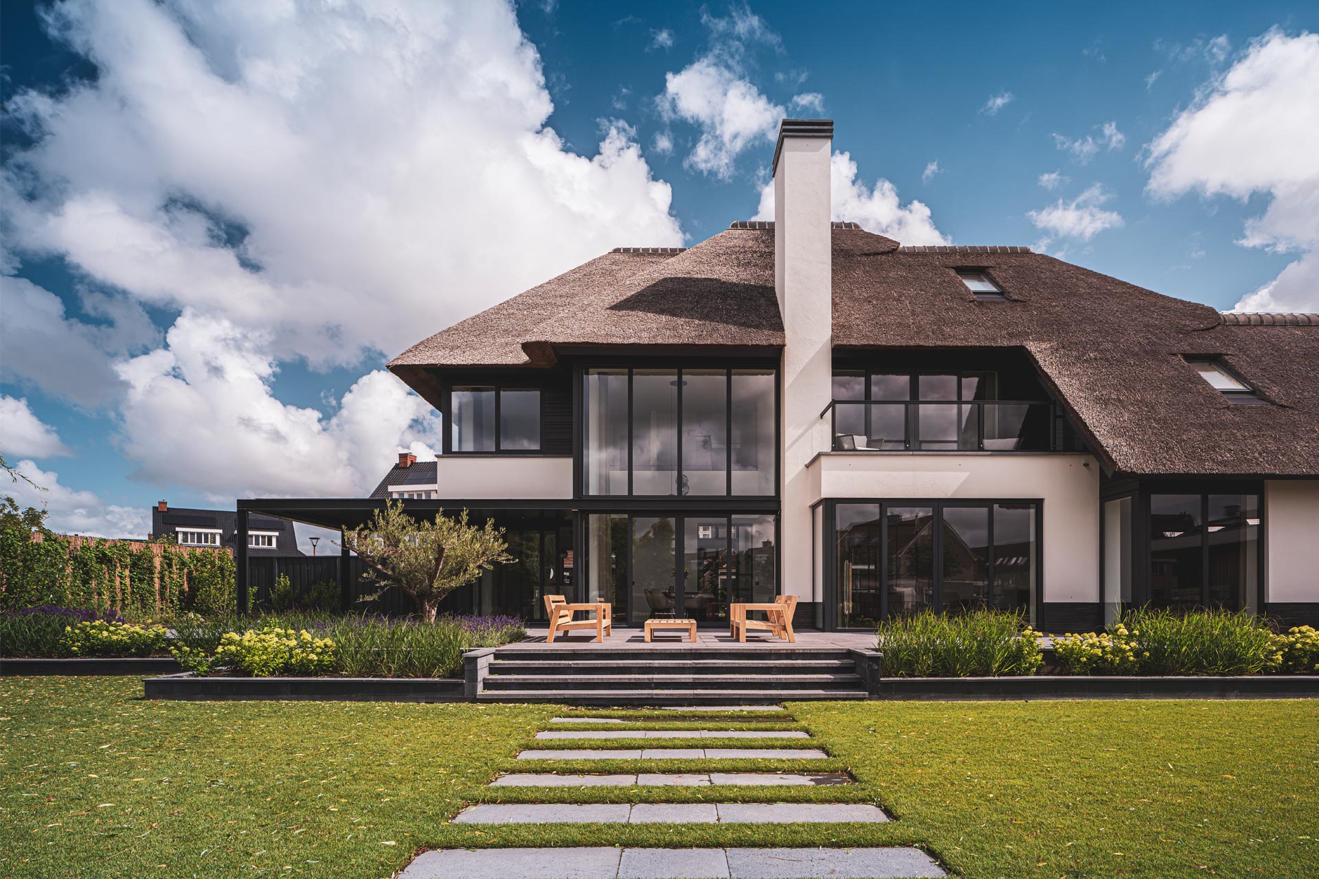 Moderne villa met rietkap, grote glaspartijen en strakke zichtlijnen in een weelderige tuinomgeving.