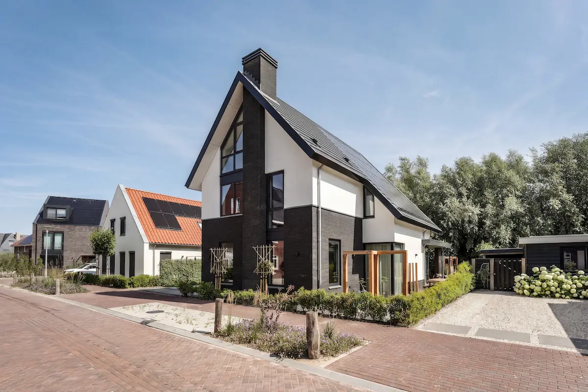 Moderne woning in Hendrik-Ido-Ambacht met steile kap, witte gevelvlakken, donker metselwerk en een verticale glaspui aan de straatzijde.