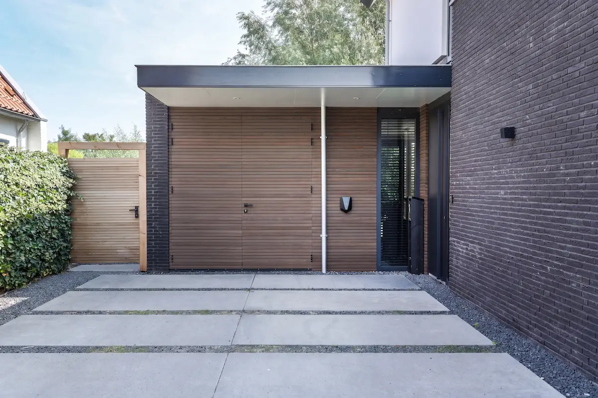 Strakke zijentree van een moderne woning in Hendrik-Ido-Ambacht met houten gevelbekleding, donker metselwerk en grote betontegels.