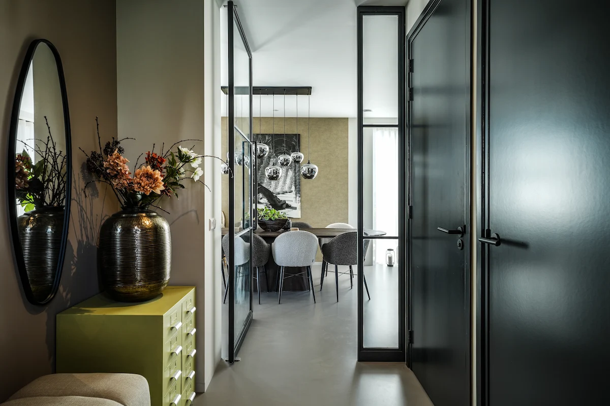 Donkere hal met stalen taatsdeur, smalle glasstroken en zicht op de lichte eetkamer in een moderne woning in Hendrik-Ido-Ambacht.