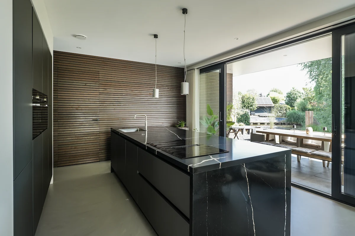 Moderne woonkeuken met donker maatwerk kookeiland, houten lattenwand en brede glazen pui naar het terras in Hendrik-Ido-Ambacht.
