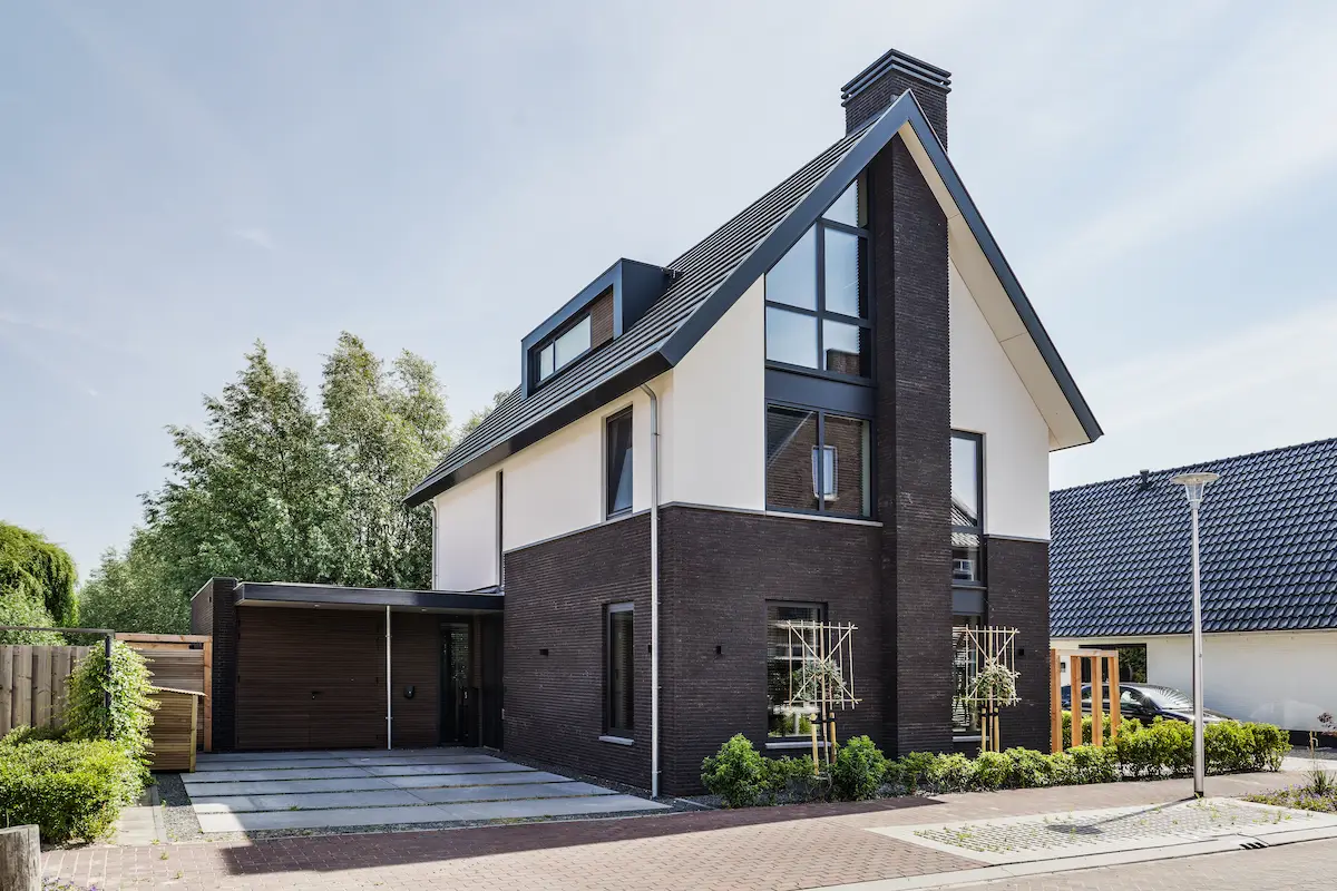 Moderne woning in Hendrik-Ido-Ambacht met steile kap, donker metselwerk, witte gevelvlakken, verticale glaspui en ge&iuml;ntegreerde carport.