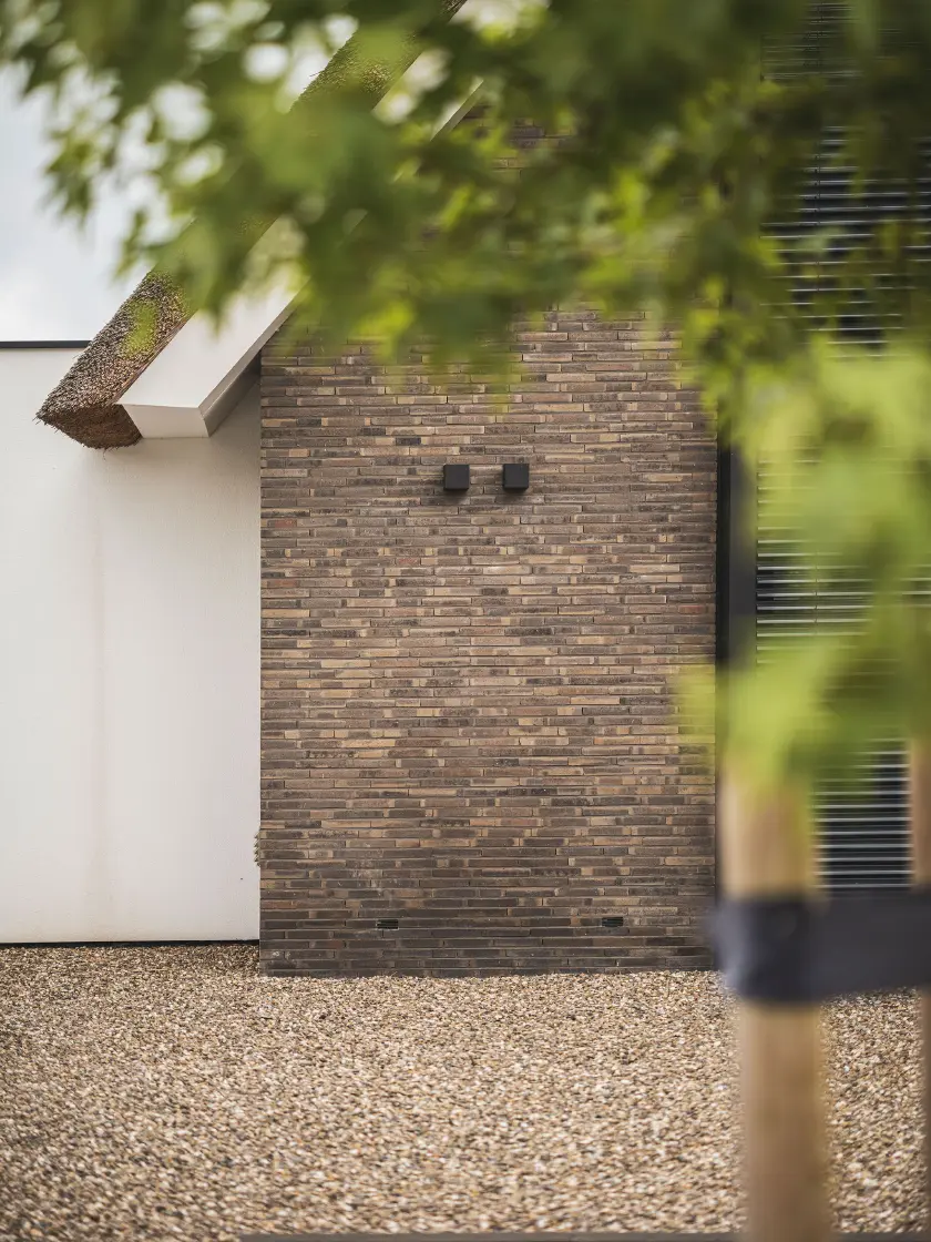 Detail van bakstenen gevel met strakke belijning en witte dakrand &ndash; duurzaam huis ontwerpen met oog voor materiaal en afwerking