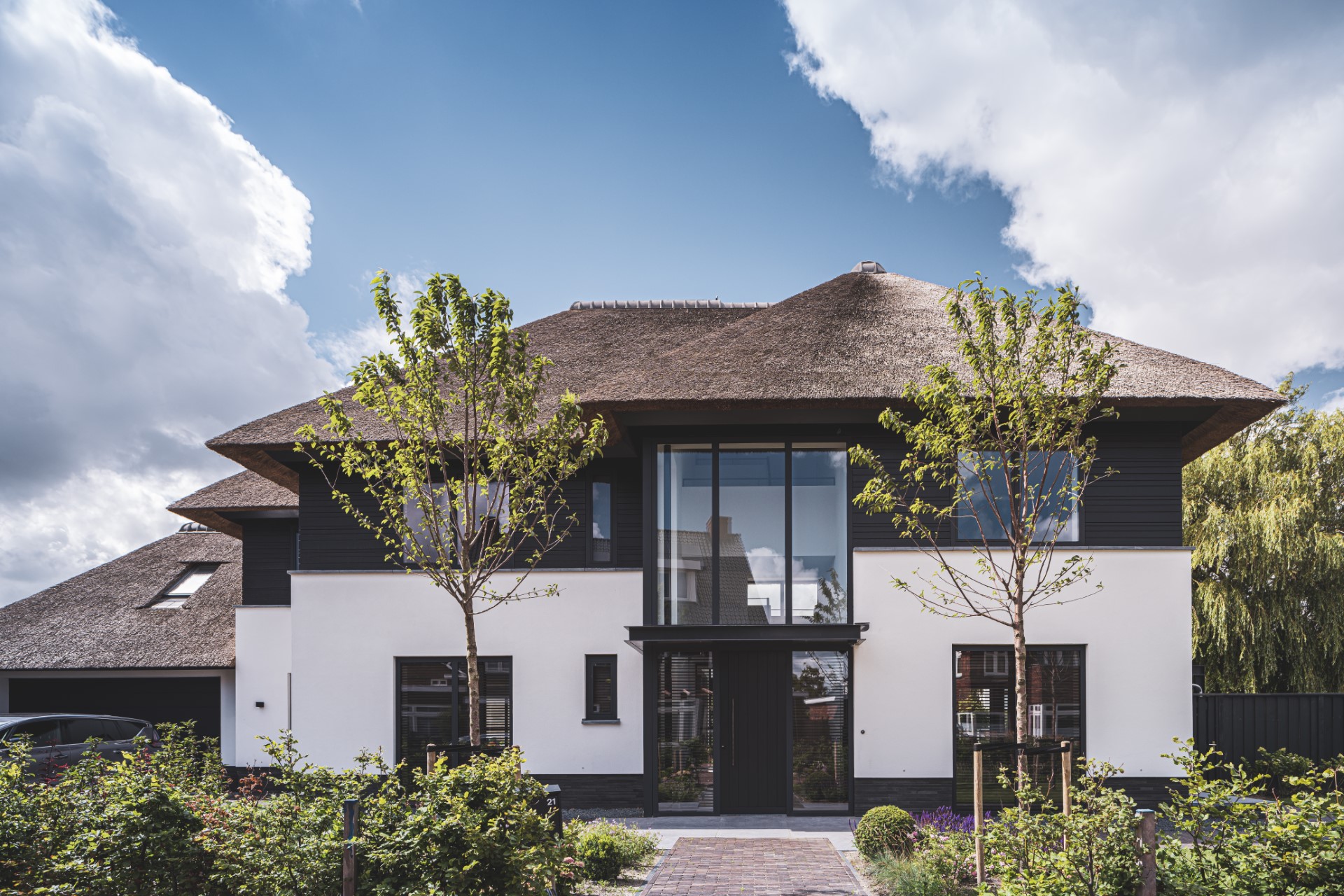 Moderne rietgedekte villa met hoge entreepartij, witte gevel en zwarte houten accenten &ndash; ontworpen door ervaren architectenbureau Bongers Architecten