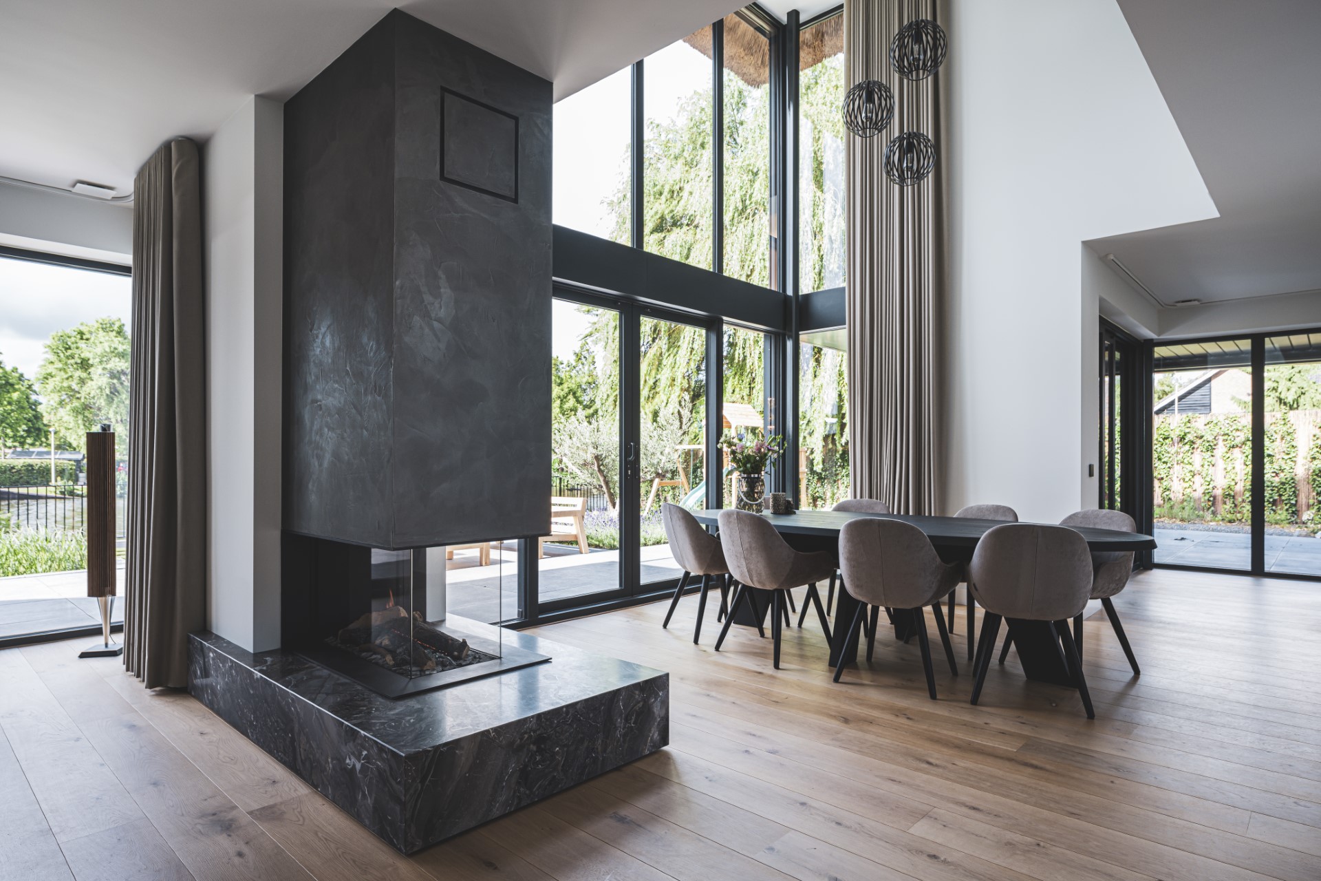 Ruimtelijke eetkamer met hoge glaspuien, open haard en eiken vloer in een moderne villa met veel licht en zicht