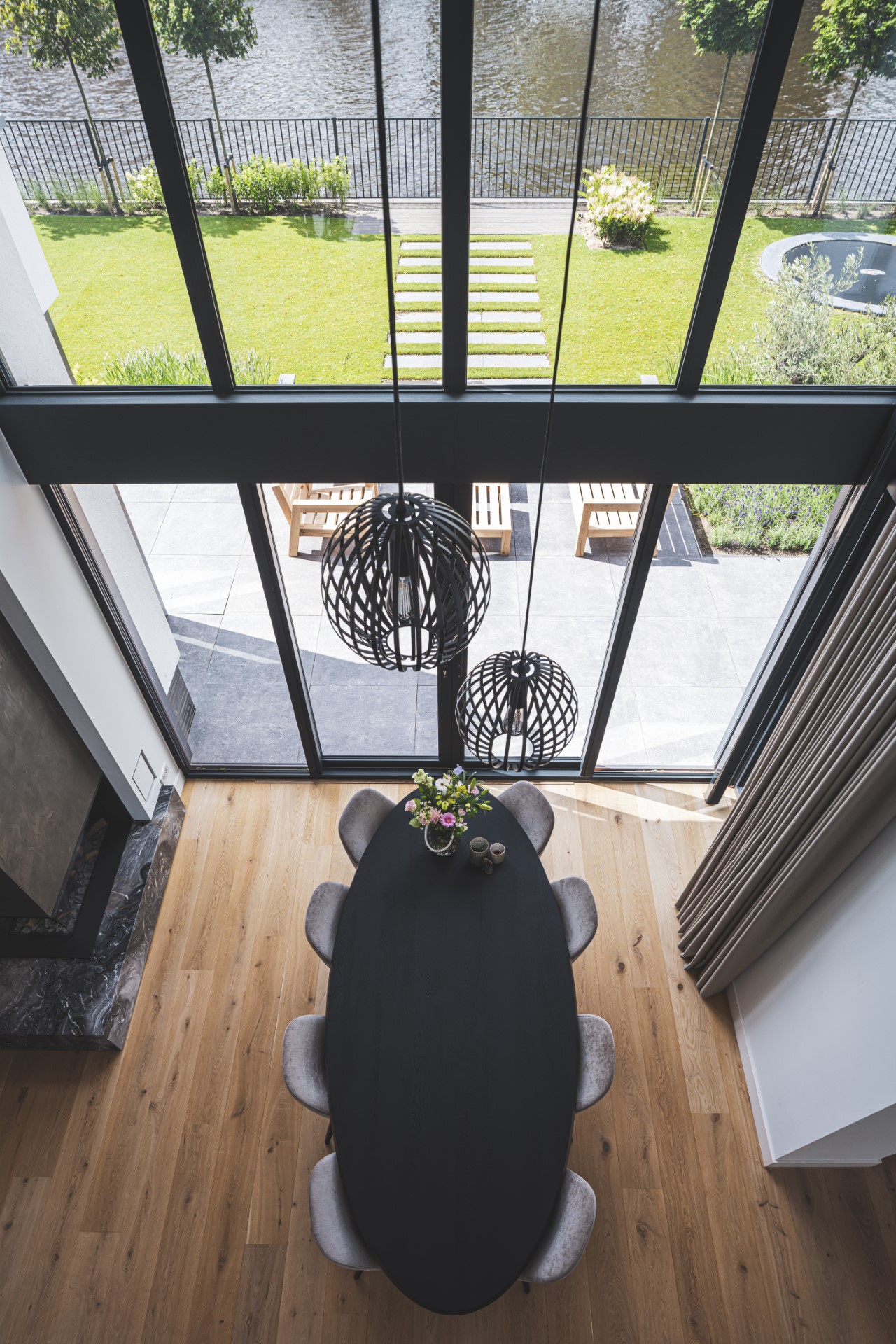 Eetkamer met vide, ovaal zwart tafelblad en uitzicht op tuin aan het water &ndash; moderne villa met licht en zicht