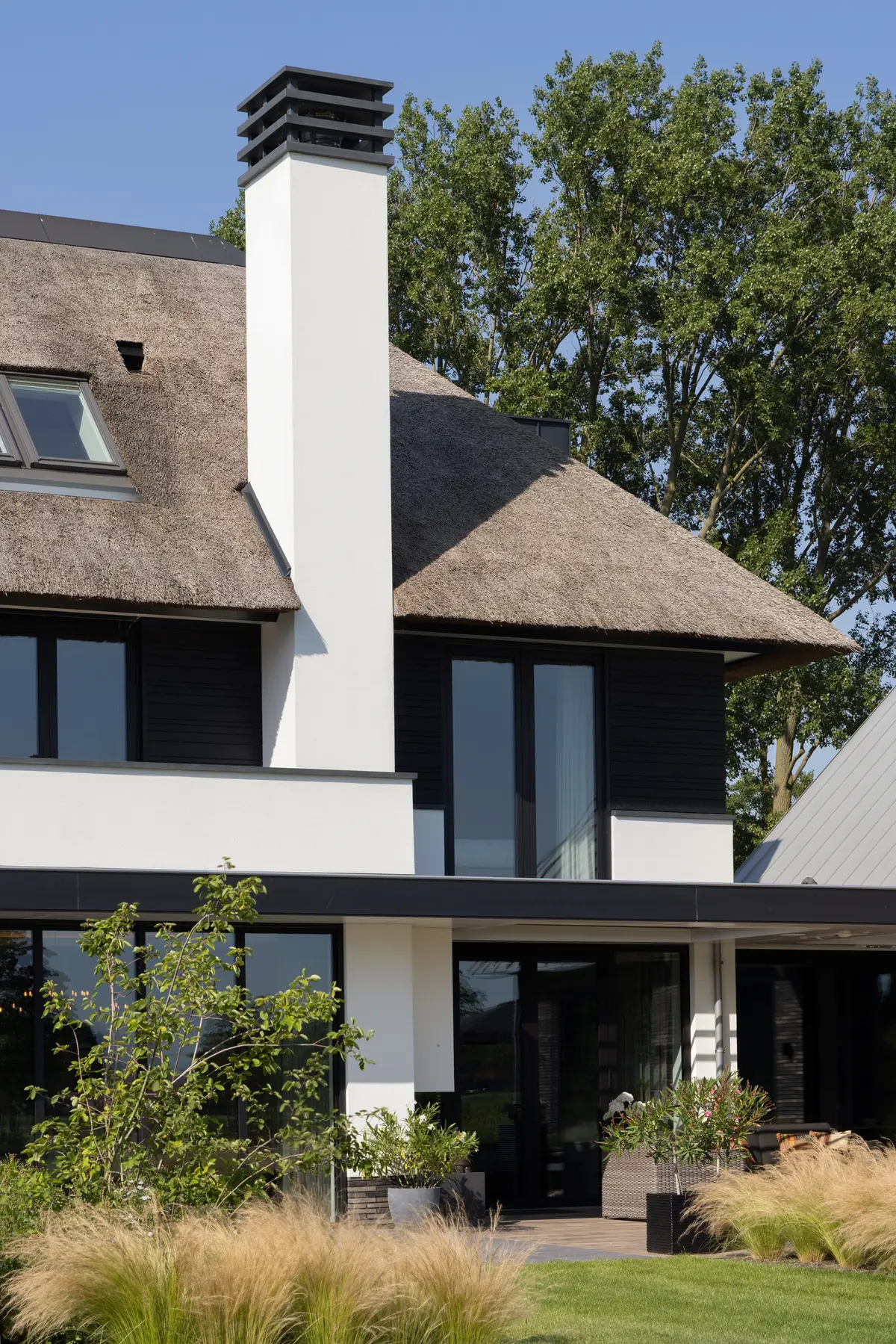 Moderne villa met rieten kap, witte schoorsteen en zwarte gevelaccenten, omringd door groen &ndash; tijdloze architectuur van Bongers Architecten.