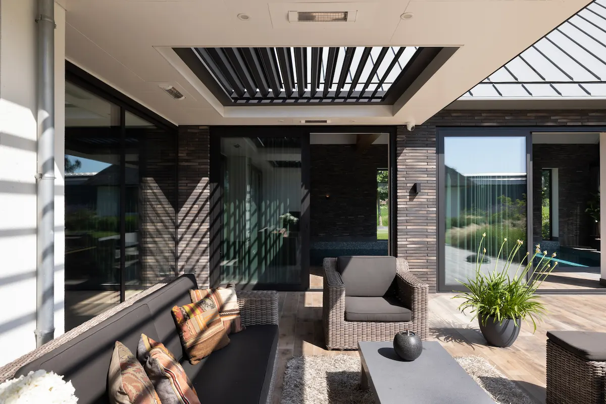 Overdekt terras met zwarte lamellen, grote glaspartijen en houten geveldetails, ontworpen als verlengstuk van een moderne villa.