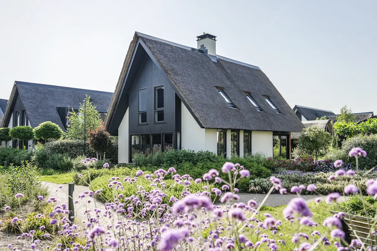 Moderne woning met rieten kap, donkere houten gevel, grote glaspartijen en bloemrijke tuin, ontworpen door architect Molenlanden.