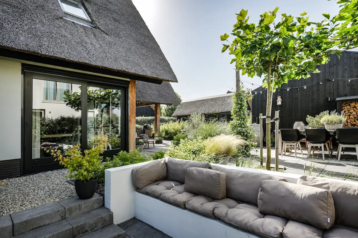 Verzonken loungeterras bij een moderne woning met rieten kap, grote schuifpui en groene tuin, ontworpen door een architect in de Drechtsteden.