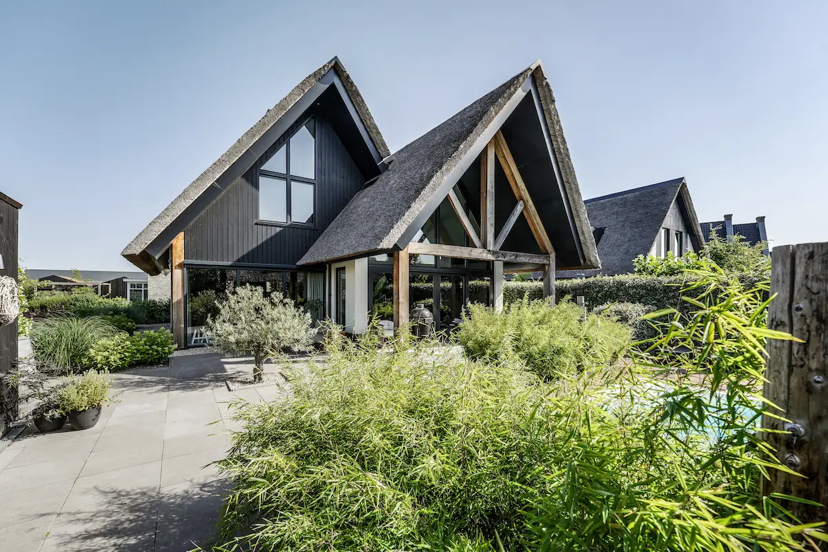 Moderne villa met rieten kappen, donkere houten gevels, houten spant en grote glaspartijen in een groene tuin, ontworpen door architect omgeving Rotterdam.