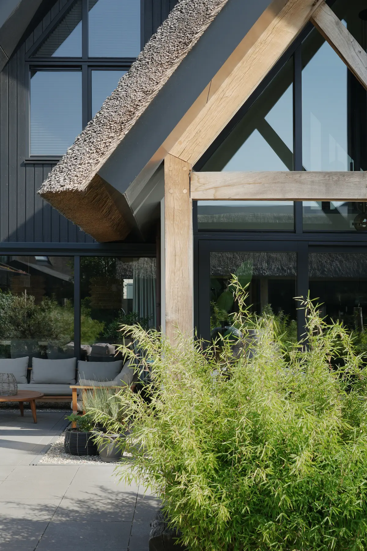 Detail van moderne villa met rieten kap, houten spant, hoge glasgevel en beschut terras, ontworpen door architect Molenlanden.