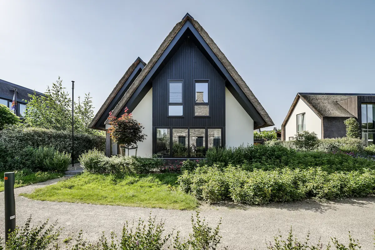 Voorgevel van moderne woning met rieten kap, donkere houten gevel en hoge ramen, omgeven door groen en ontworpen door architect Drechtsteden.