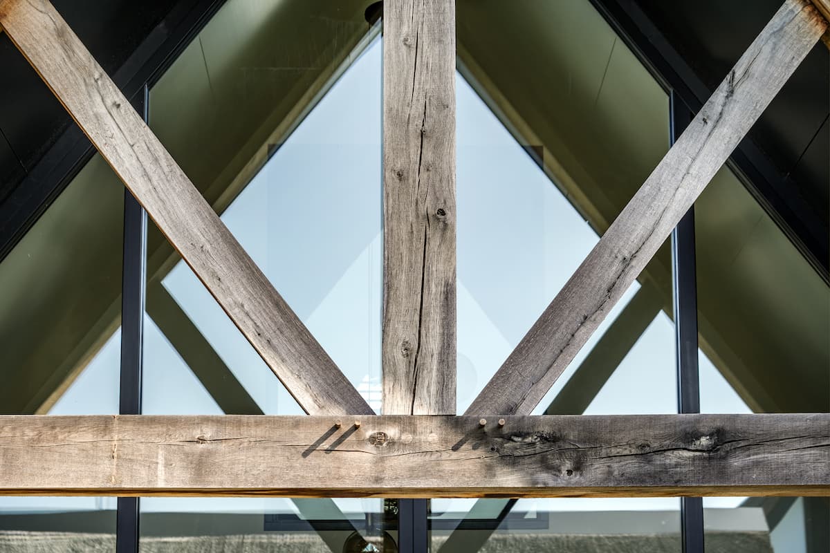 Detail van robuuste houten spanten voor een hoge glazen topgevel, met zicht op de rieten kap van een moderne villa door architect omgeving Rotterdam.