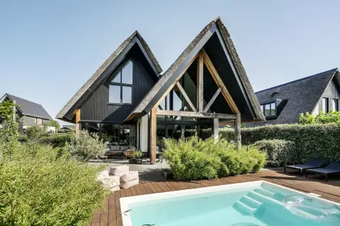 Moderne villa met rieten kappen, houten spanten, grote glaspartijen en zwembad in een groene tuin, ontworpen door architect in Oud-Alblas.