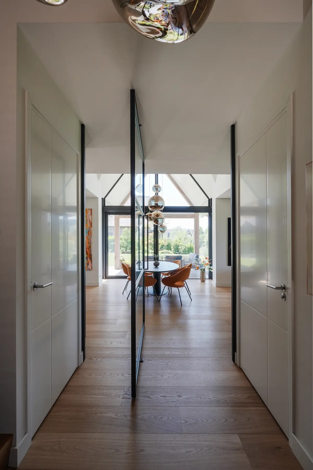 Lichte hal met glazen taatsdeur, houten vloer en zicht op de eetkamer met grote ramen in een minimalistische woning van architect Drechtsteden.