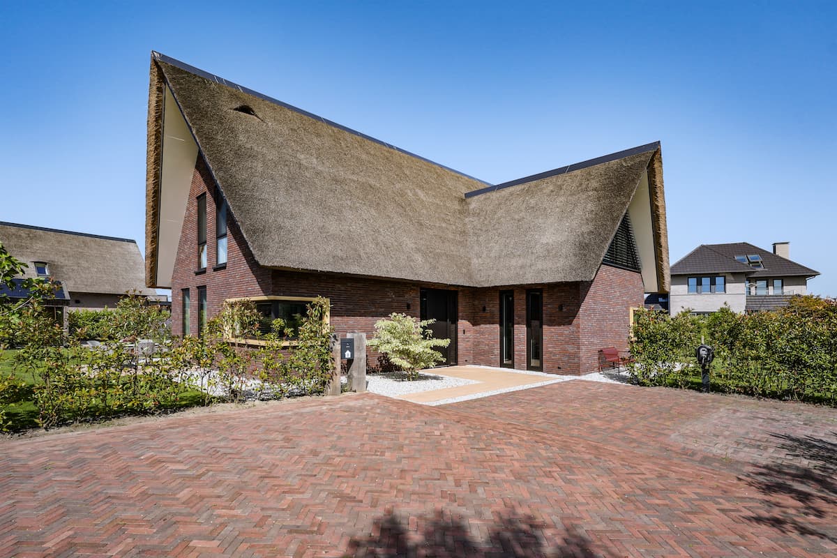 Moderne villa met asymmetrisch rieten dak, donkere baksteen en beschutte entree aan een ruim erf, ontworpen door architect in Oud-Alblas.