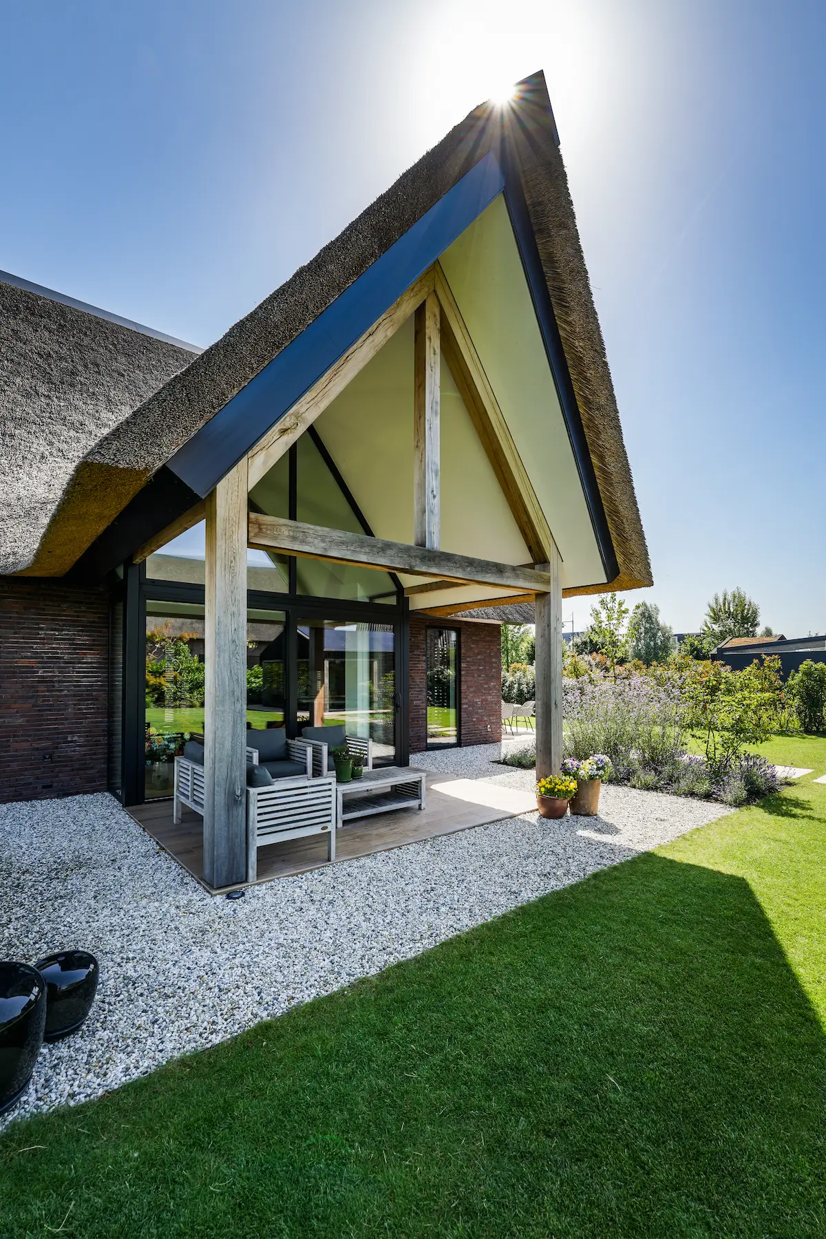 Detail van een moderne villa met rieten kap, houten spanten en glazen gevel, ontworpen voor licht en tuinzicht door architect Molenlanden.