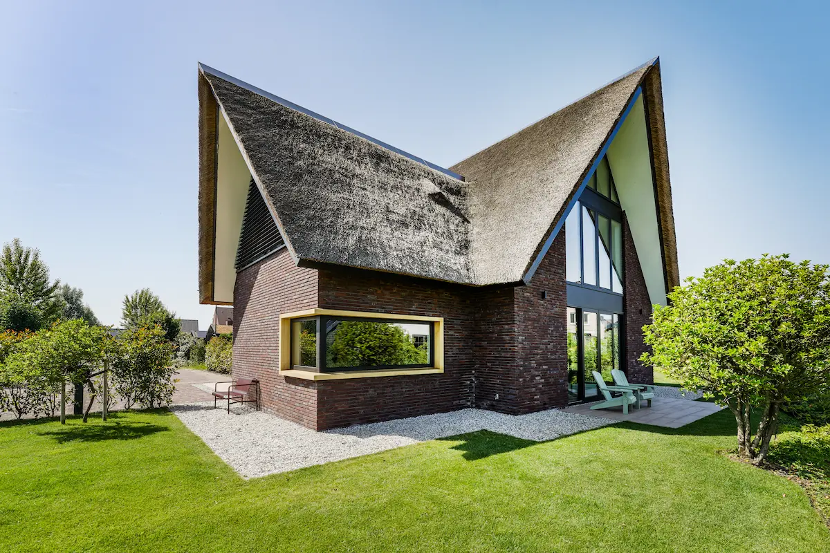 Moderne villa met sculpturale rieten kap, donkere baksteen, hoekraam en hoge glasgevel, ontworpen door architect omgeving Rotterdam.