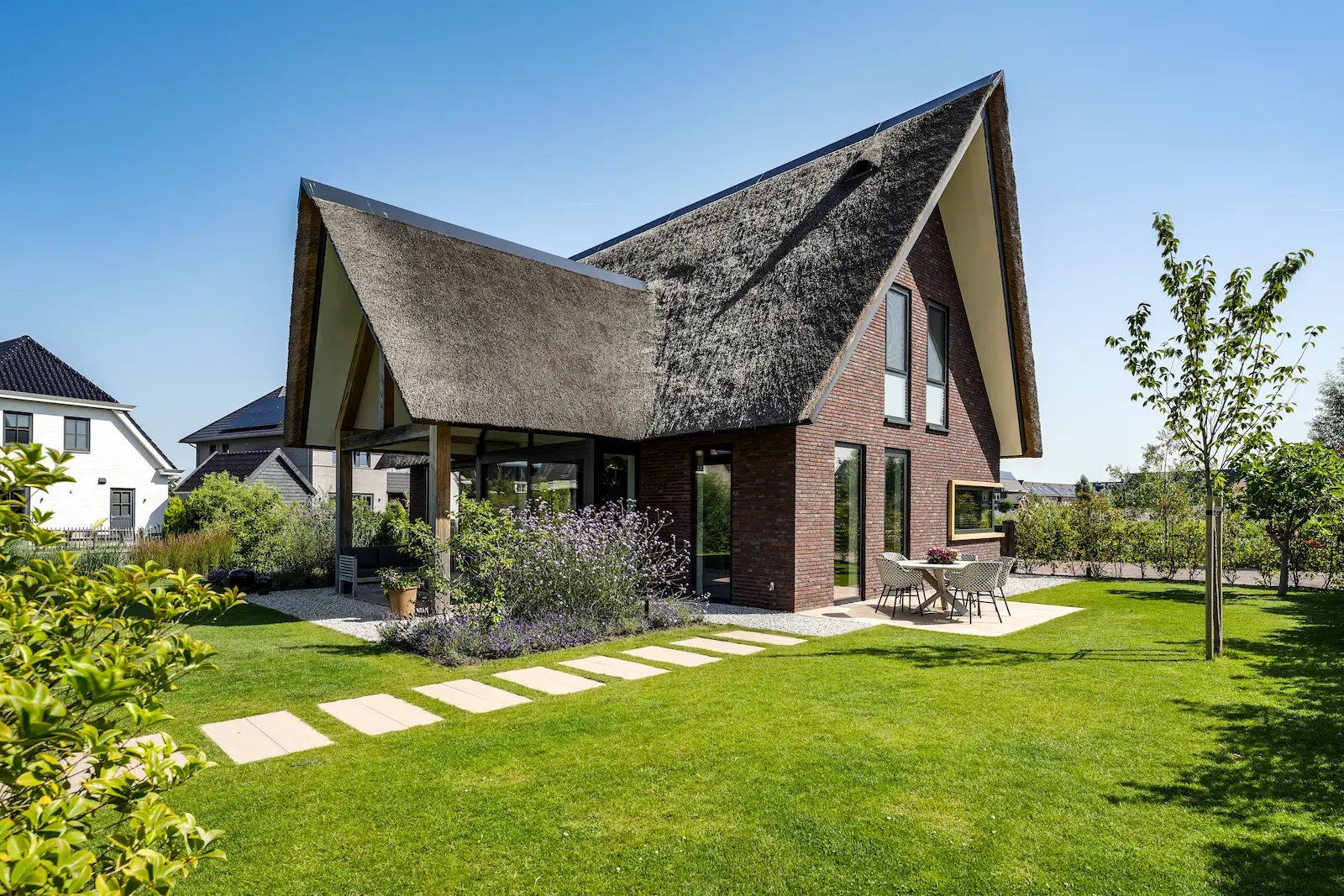 Moderne villa met sculpturale rieten kap, donkere baksteen en glazen tuingevel, omgeven door groen en ontworpen door architect in Oud-Alblas.