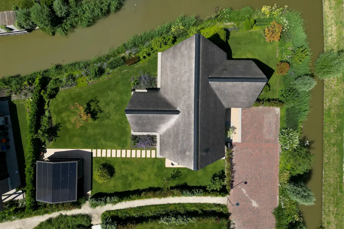 Luchtfoto van een moderne villa met donkere dakvlakken, groene tuin en ligging aan het water, ontworpen door architect in Oud-Alblas.