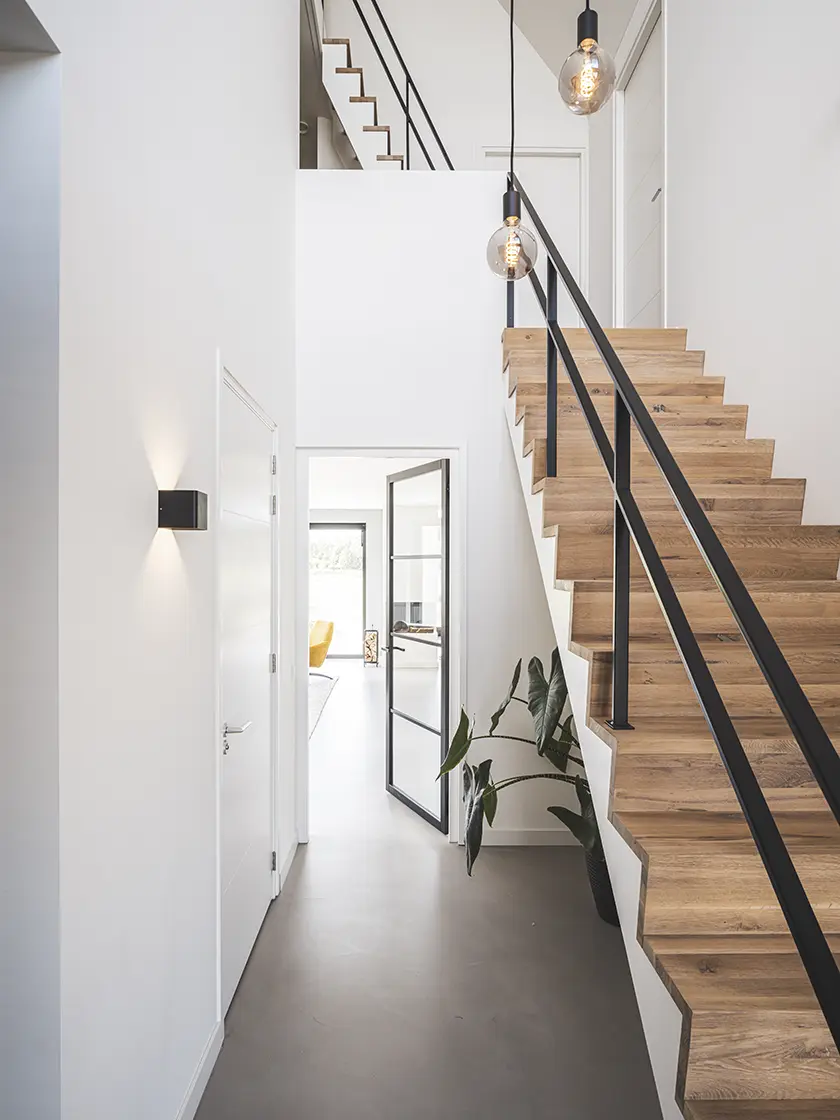 Moderne hal met open houten trap, zwart stalen leuning en vide in een lichte woning van architect Molenlanden.