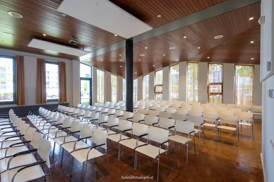Lichte kerkzaal van Ichtuskerk in Alblasserdam met houten plafonds, grote ramen en flexibele opstelling.