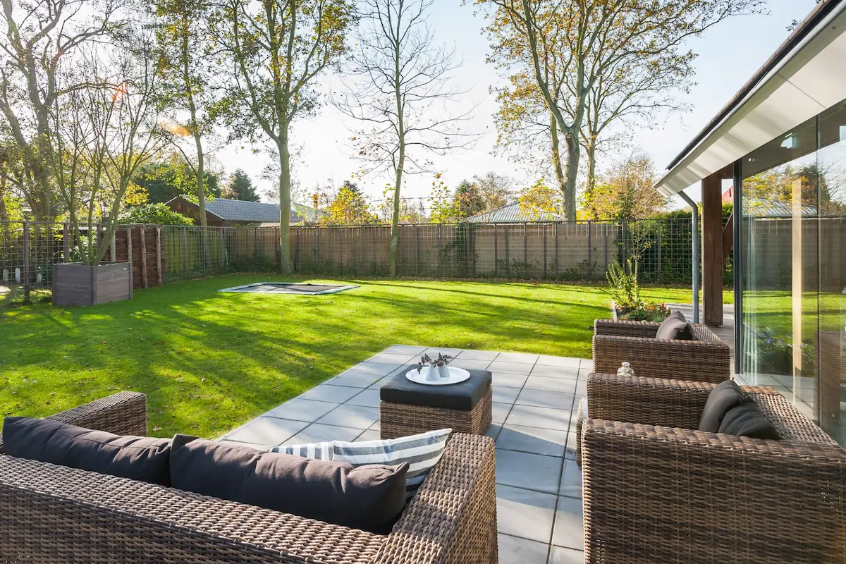 Zonnig terras met loungeset en ruime tuin bij recreatiewoning &ndash; architect woningontwerp met focus op buitenleven en lichtinval.
