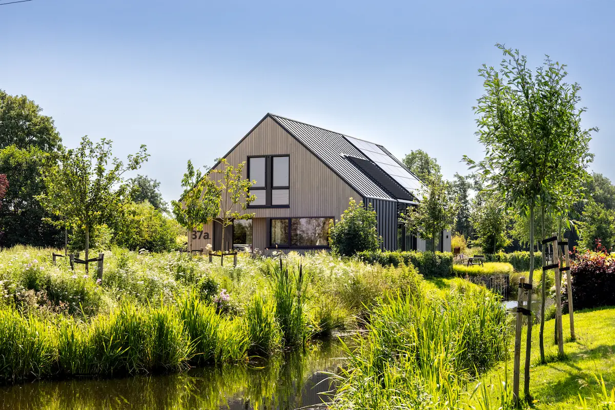 Moderne villa met verticale houten gevel, zonnepanelen en grote ramen, omgeven door een natuurlijke watertuin van architect in Oud-Alblas.