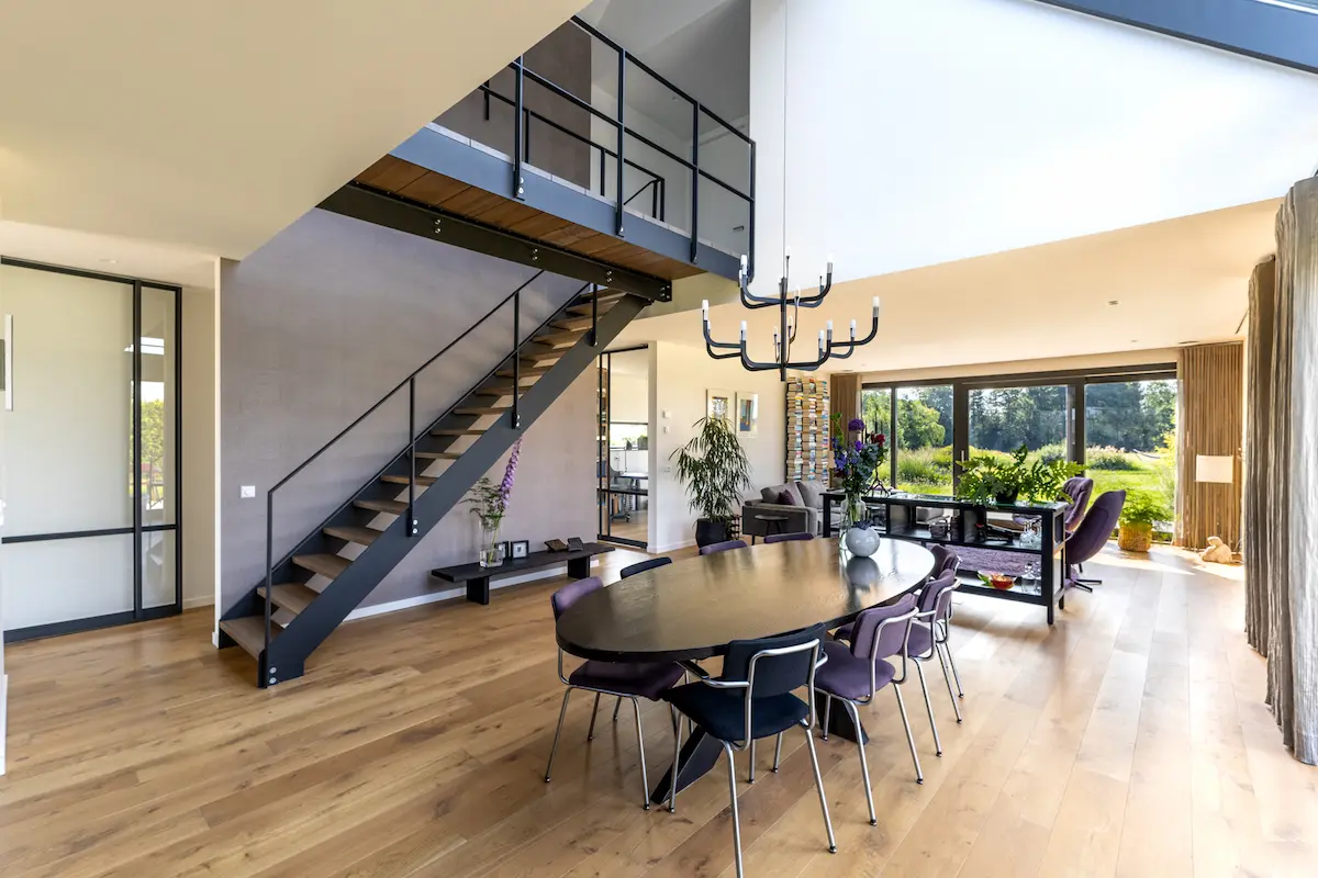 Ruimtelijke eetkamer met vide, stalen trap, houten vloer en grote glaspartijen in een moderne villa, ontworpen door architect omgeving Rotterdam.