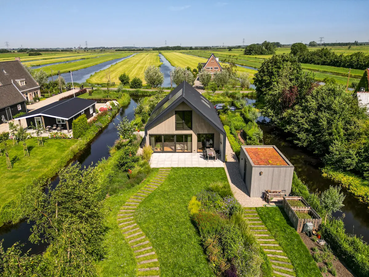 Luchtfoto van een moderne villa met houten gevel, grote glaspartij en groene tuin aan het water, ontworpen door architect Molenlanden.
