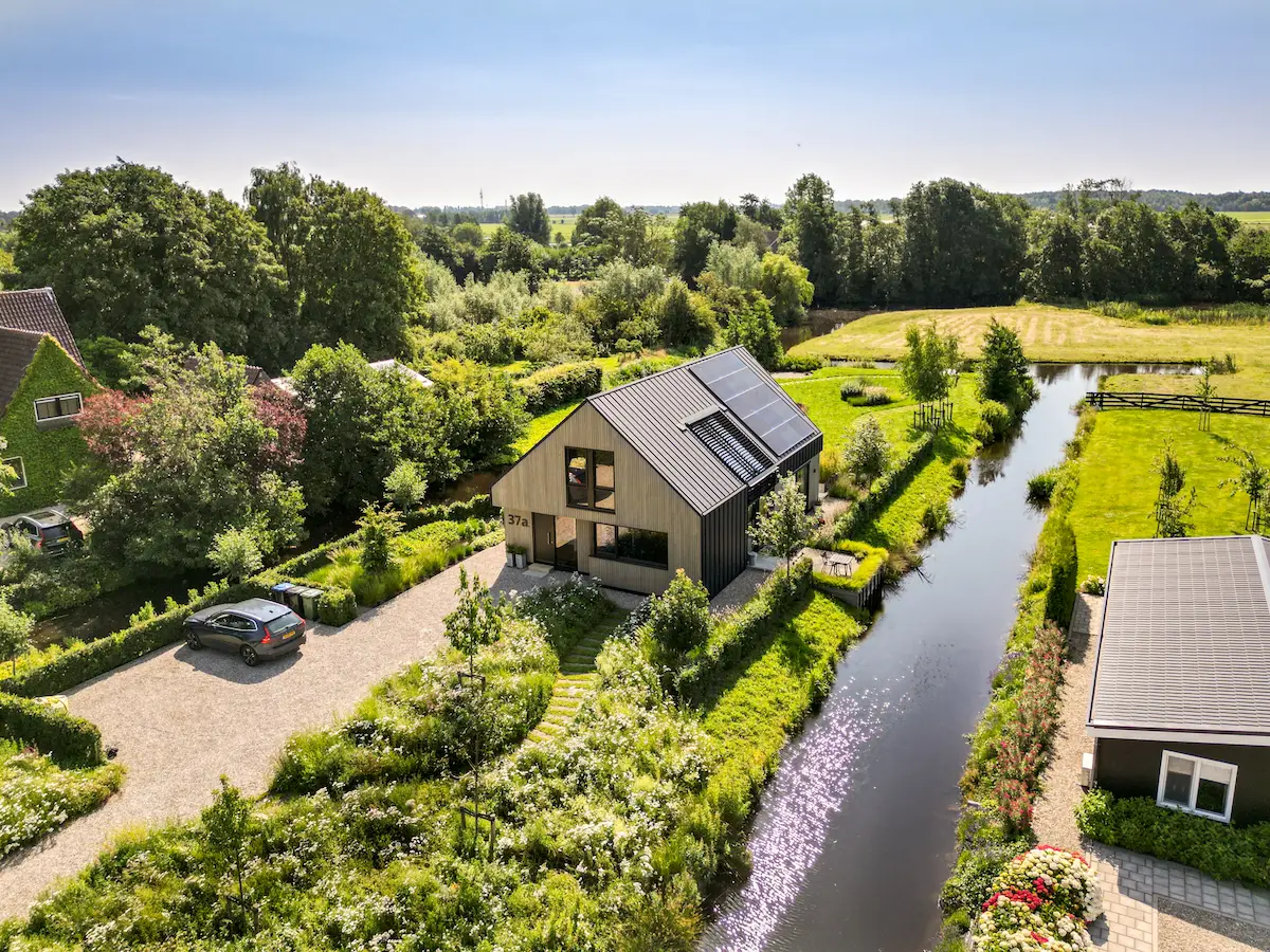 Luchtfoto van een moderne houten woning met zonnepanelen, groene tuin en ligging aan het water, ontworpen door architect Molenlanden.